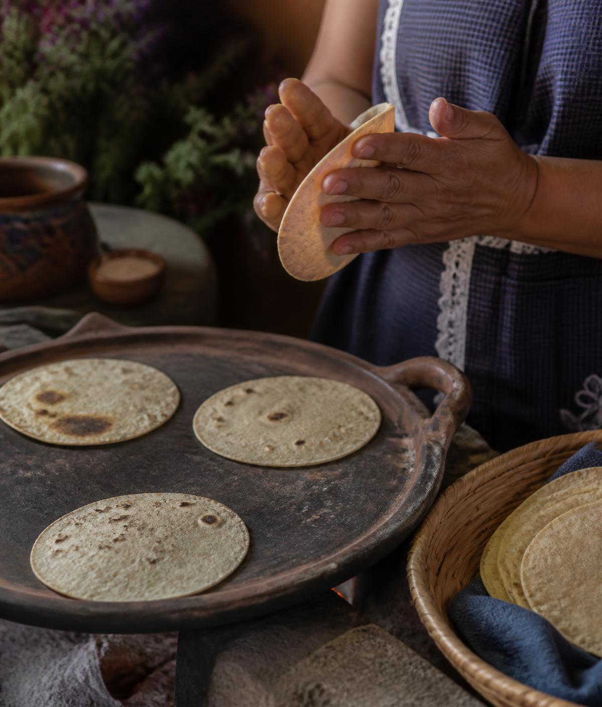 Manos elaborando tortillas de maíz a mano sobre un comal de barro