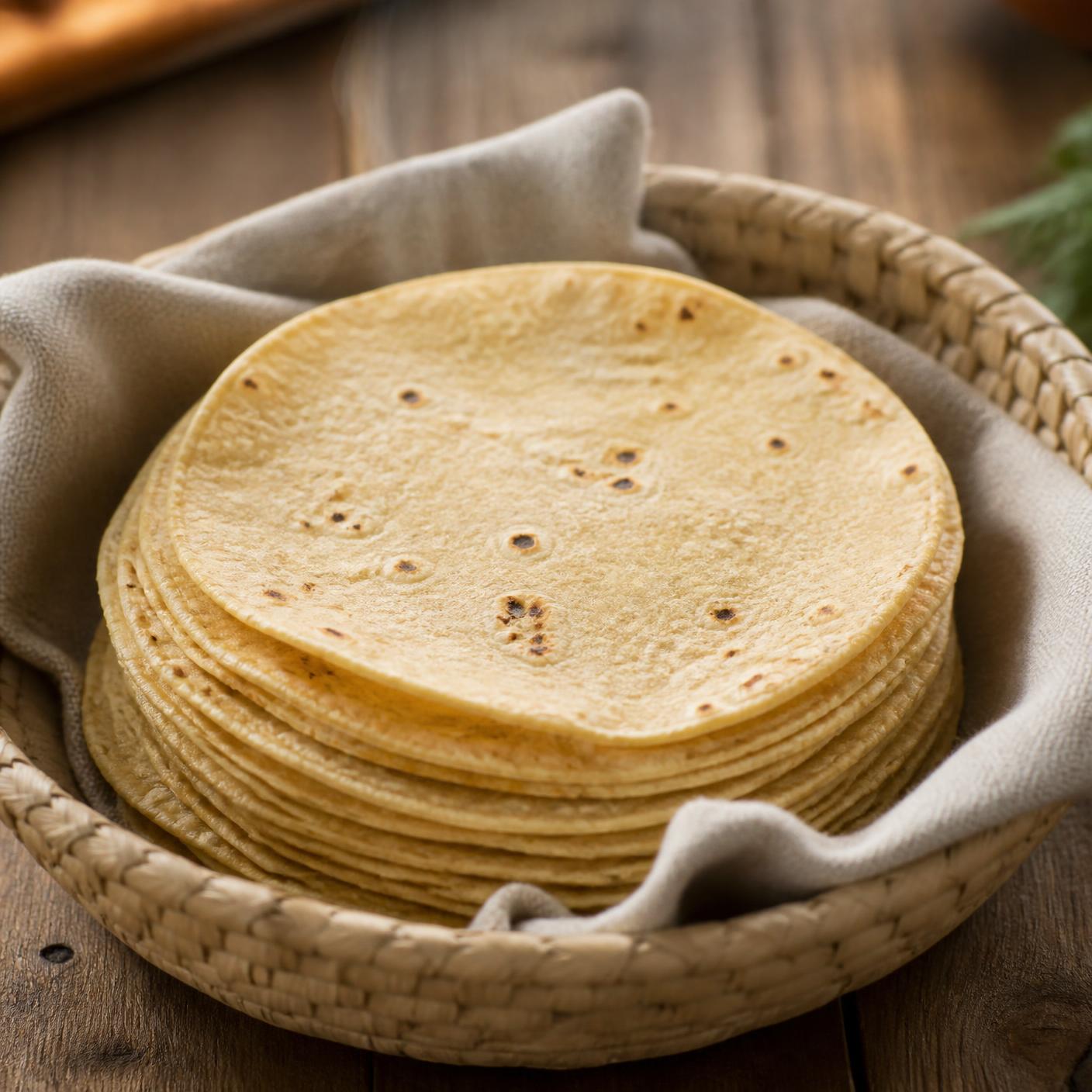 Tortillas de maíz suaves apiladas en una canasta de palma con manta de tela